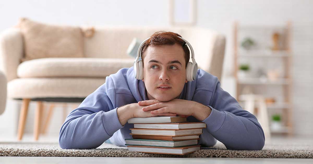 Mann hört Hörbuch mit Kopfhörern und liegt auf Büchern – Verbindung von Lesen und Stimme