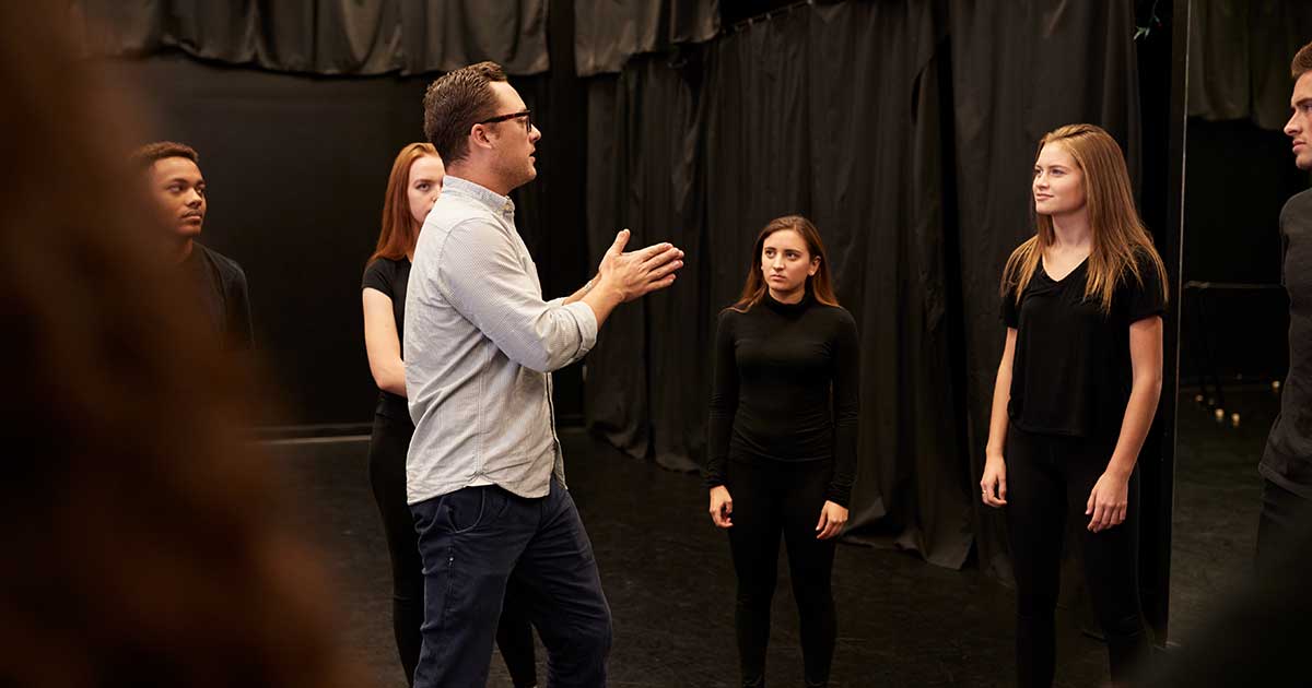 Schauspieltrainer gibt Anweisungen an eine Gruppe junger Schauspielschüler auf der Theaterbühne