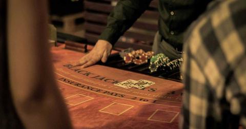 Casino-Dealer am Blackjack-Tisch mit Chips und Spielern im Vordergrund
