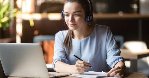 Junge Frau mit Headset macht Notizen am Laptop