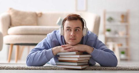 Mann hört Hörbuch mit Kopfhörern und liegt auf Büchern – Verbindung von Lesen und Stimme