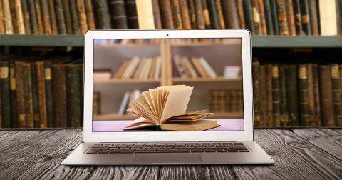 Laptop mit geöffnetem Buch auf dem Bildschirm vor einem Bücherregal – Symbol für den Wandel von analoger Literatur zur digitalen Kommunikation.