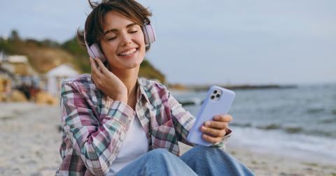 Frau sitzt am Strand und hört ein Hörbuch