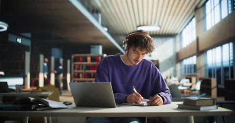 Student arbeitet konzentriert in der Bibliothek an Laptop und Notizen für seine Masterarbeit.