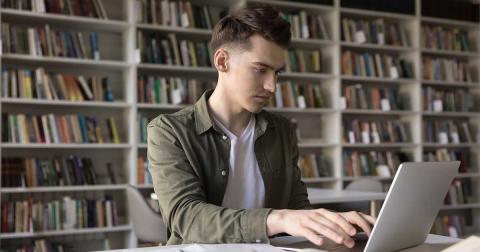 Student schreibt wissenschaftliche Arbeit am Laptop in einer Bibliothek