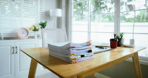 Stapel geordneter Studienunterlagen auf einem aufgeräumten Schreibtisch mit Laptop und Tageslicht