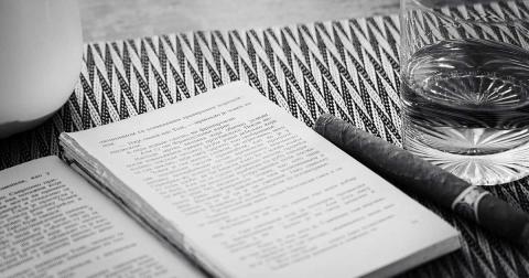 Aufgeschlagenes Buch mit Zigarre und Glas in einer ruhigen, symbolischen Schwarz-Weiß-Szene